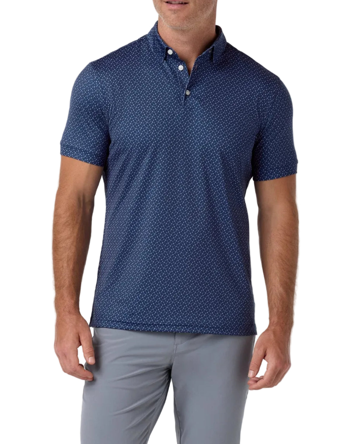 A man modeling a short-sleeve polo shirt with a navy blue and white micro-dot pattern, paired with gray trousers, against a light gray studio background.